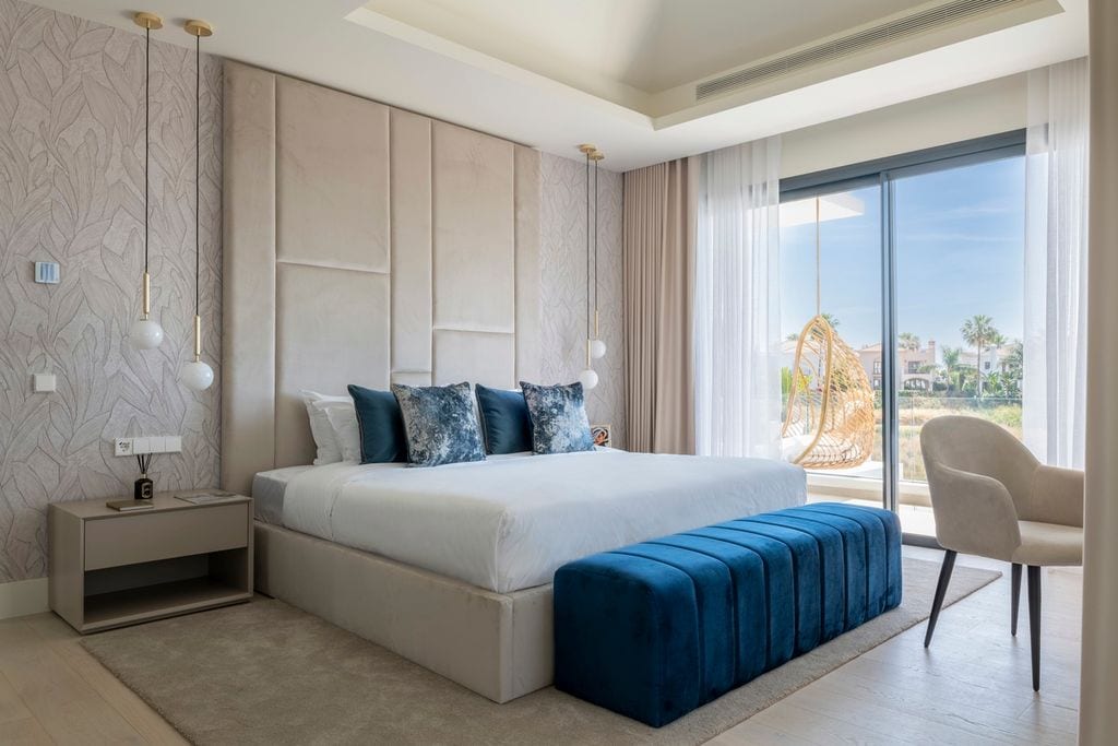 Dormitorio principal de una casa en Estepona (Málaga) diseño de Alexandra Studio, quien crea el cabecero tapizado, el cual va acompañado de un papel texturizado de Arte, lámparas suspendidas de Nuura
