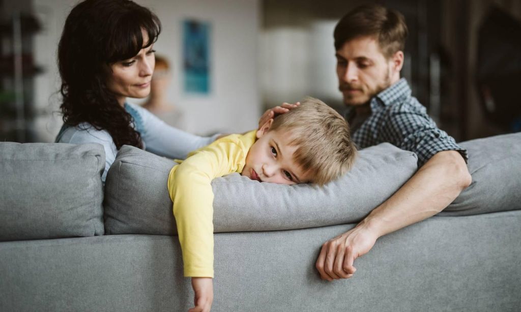 ni o aburrido apoyado en el respaldo del sof con padres al lado que le animan