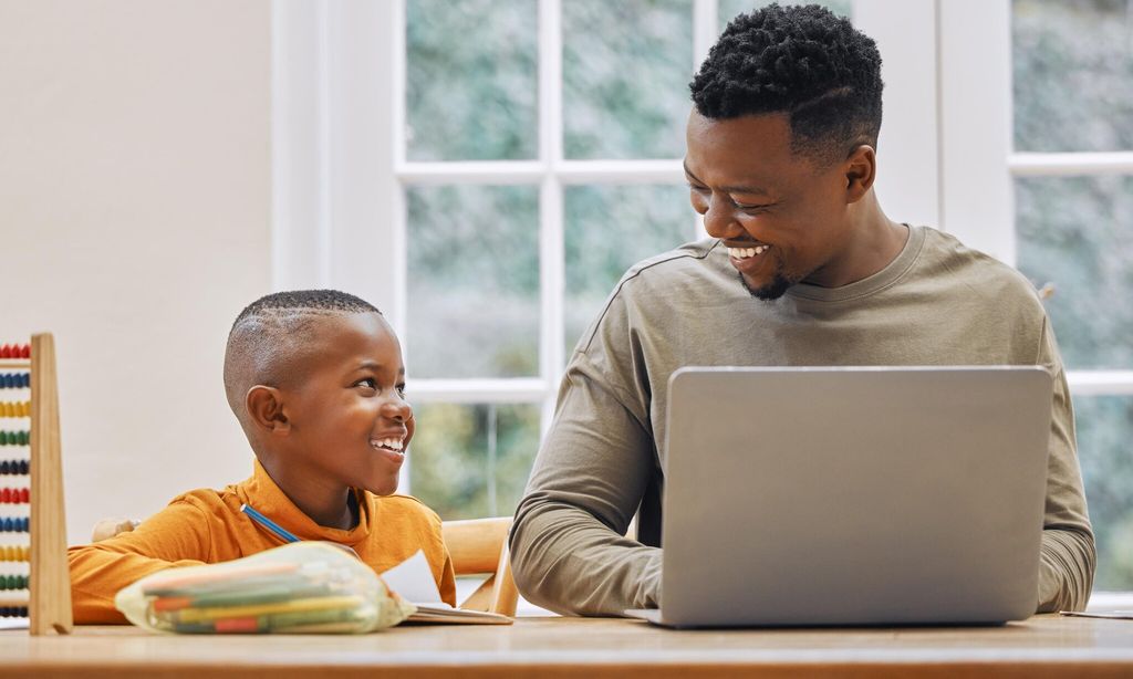 shot of a young father using a laptop while his son does homework at home