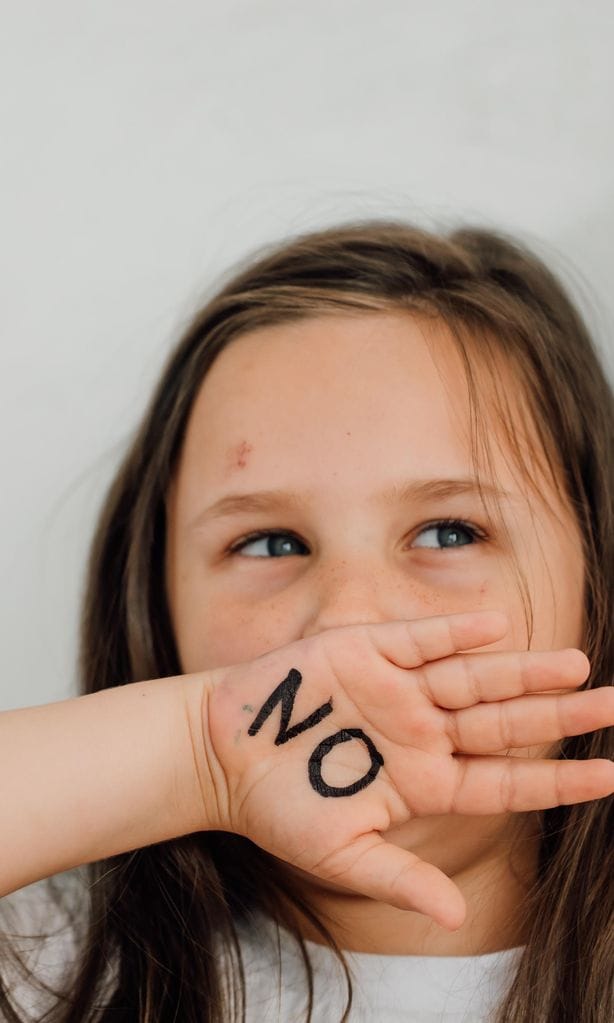 Niña con mano en la boca con un \'no\' pintado porque no quiere comer