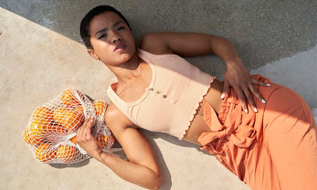 Short hair Woman laying down on the floor holding a bag full of oranges with half of the body in shadow