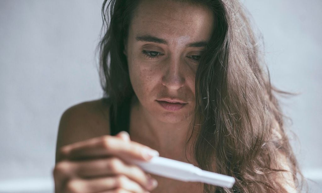 Woman holding pregnancy test with depressed worried face expression