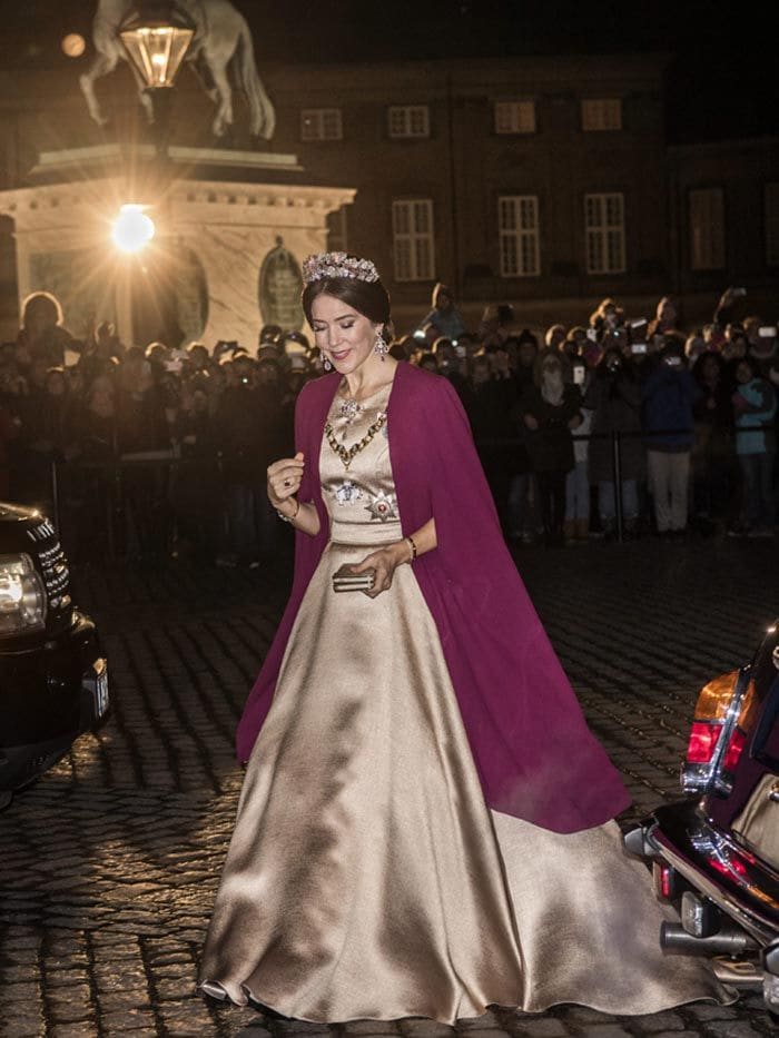 La esposa del Príncipe heredero vistió de oro la ocasión con un elegante vestido del diseñador Jesper Hovring, que combinó con una capa de color amaranto, la prenda que reina en la Cortes Reales, y con un clutch de Judith Leiber
