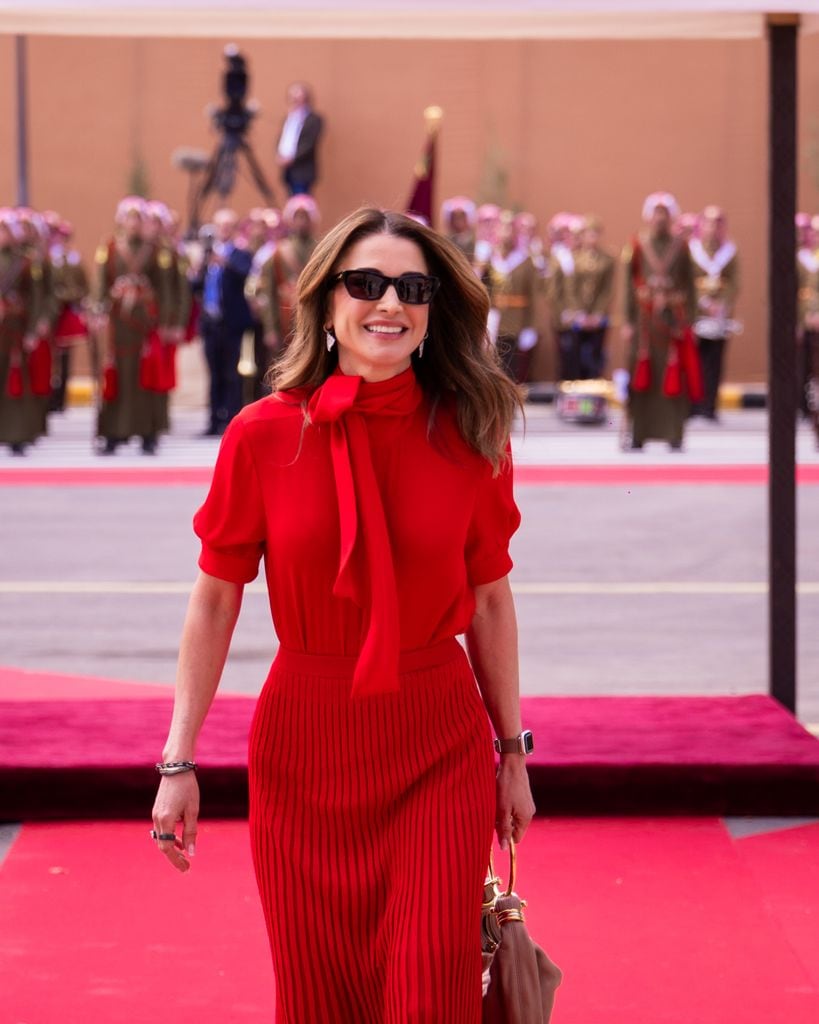 Rania de Jordania con conjunto rojo de blusa y falda plisada con gafas de sol