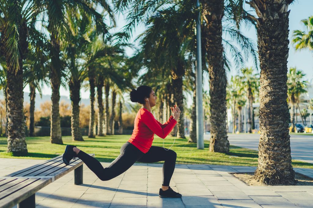 mujer haciendo lunges apoyada en un banco, al aire libre