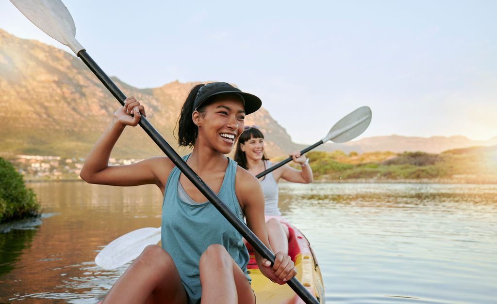 dos mujeres sonrientes haciendo kayak en verano