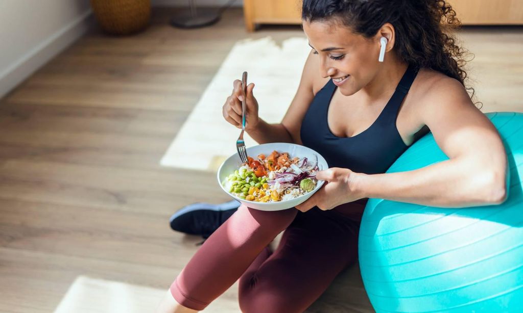 mujer apoyada en pelota de pilates comiendo una ensalada