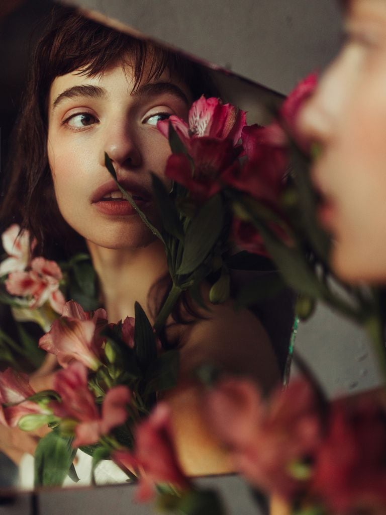 Mujer mirándose al espejo con un ramo de flores rosas