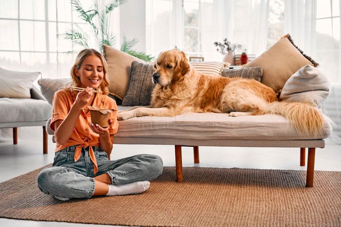 mujer cenando en el suelo mientras la mira su perro