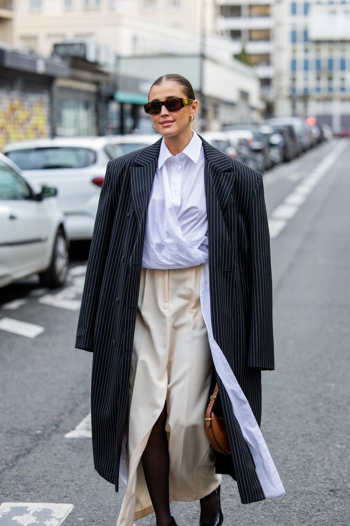 Darja Barannik lleva abrigo de rayas blanco negro, falda beige, camisa blanca de botones, medias, gafas de sol, pendientes, tacones, bolso de Prada en marrón fuera de Viktor&Rolf durante la Alta Costura Primavera/Verano 2024 como parte de la Semana de la Moda de París el 24 de enero de 2024 en París, Francia.