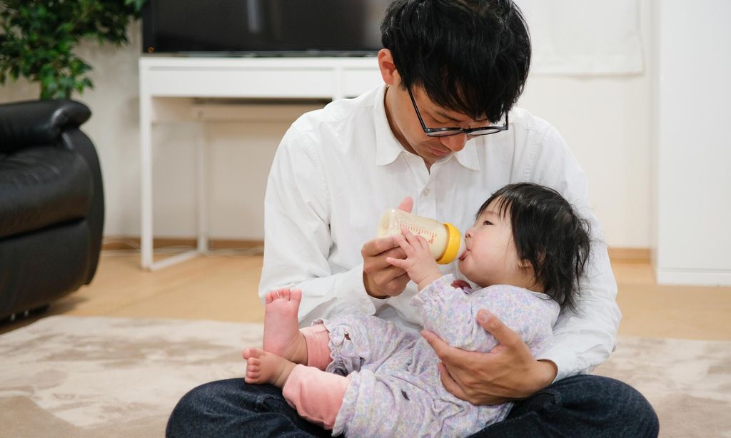 father feeding milk to baby at home