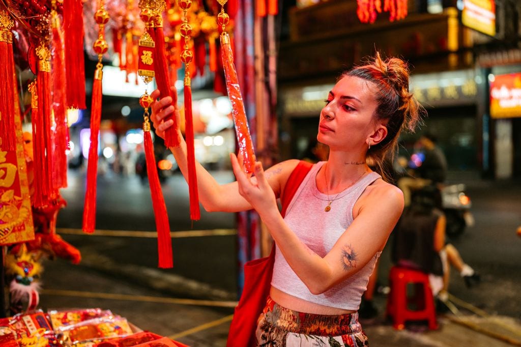 Beautiful young woman shopping for Chinese New Year decorations in Chinatown in Bangkok in Thailand at night.