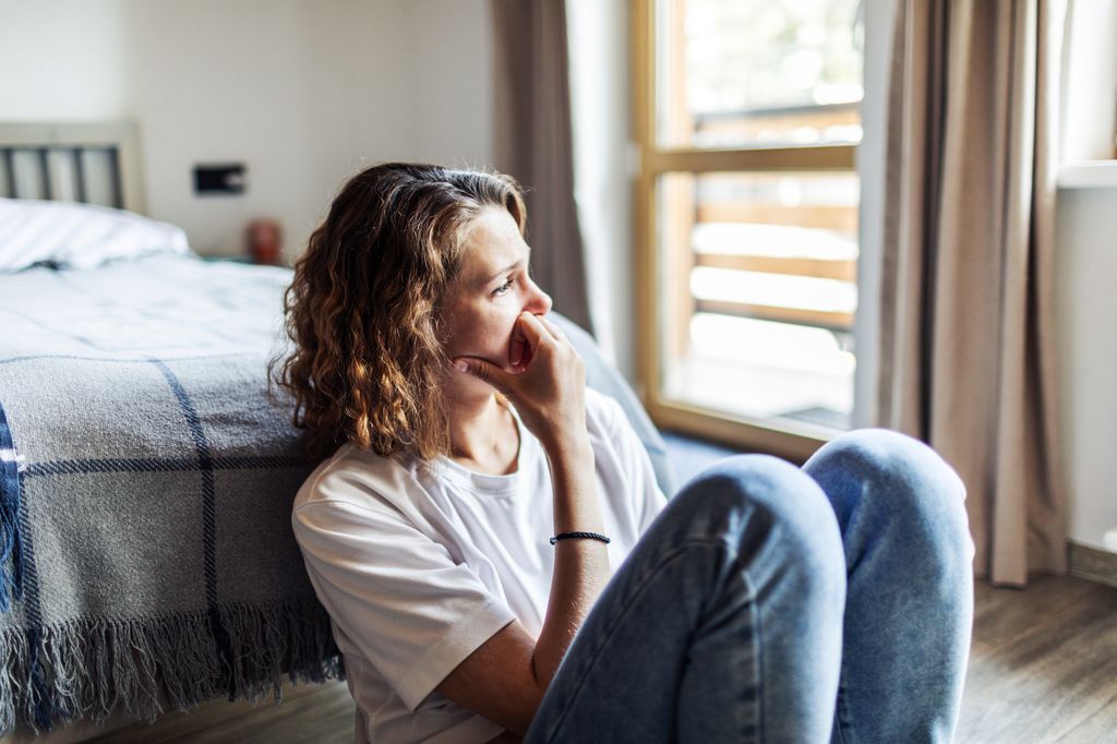 mujer triste sentada en el suelo a los pies de la cama