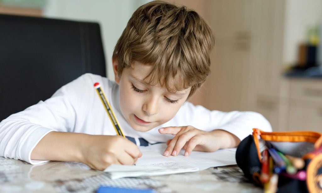 tired kid boy at home making homework writing letters with colorful pens