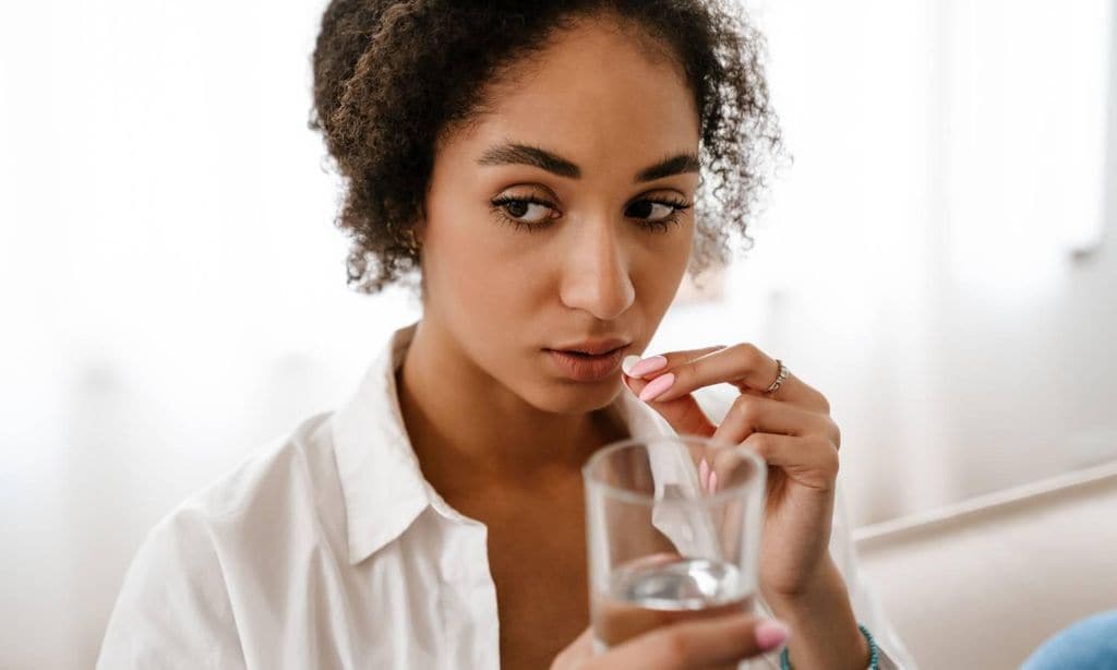 mujer con vaso de agua en la mano tomando una pastilla