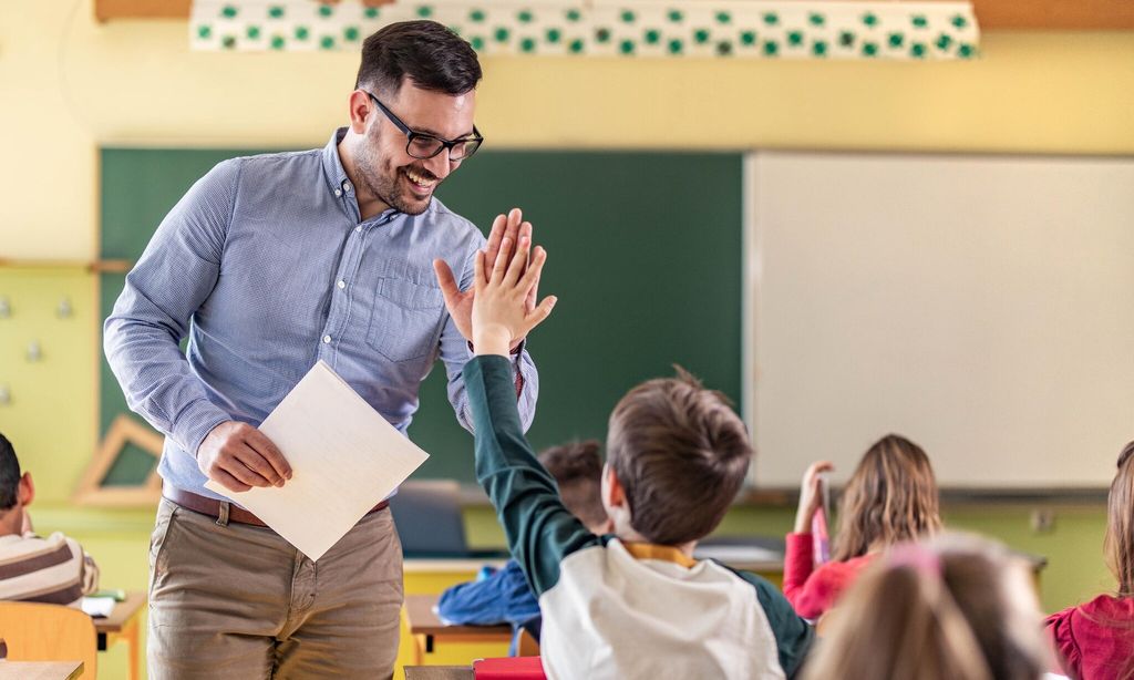 happy teacher and schoolboy giving each other high five on a class 