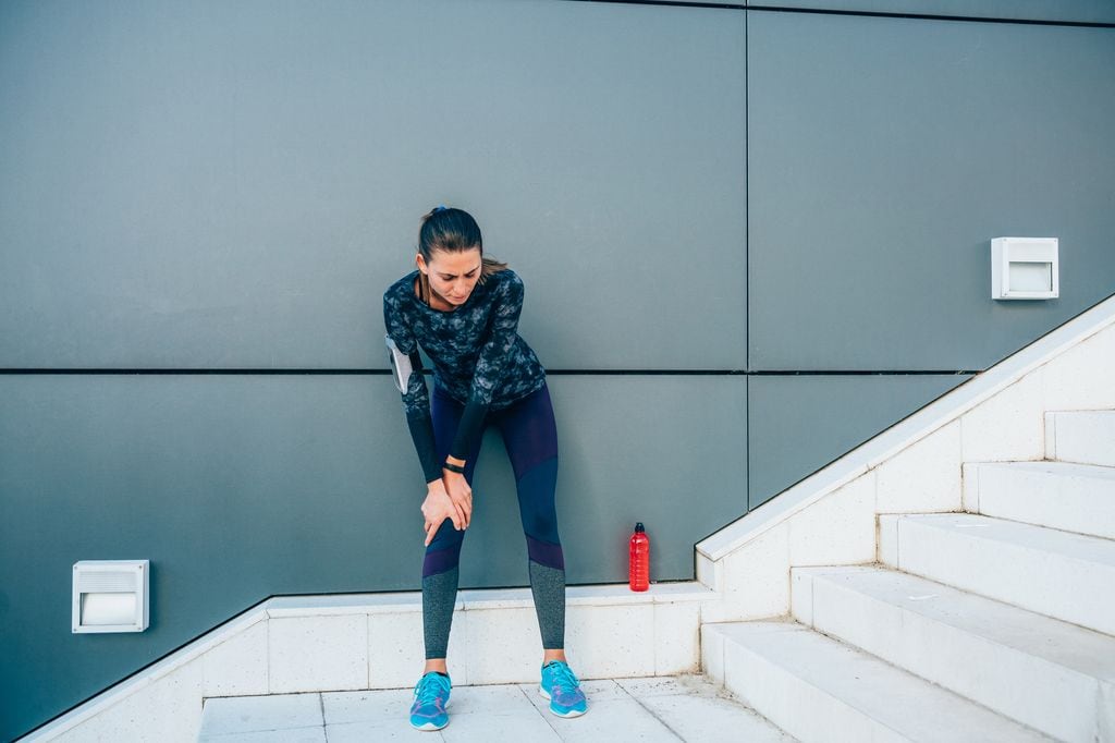 mujer con dolor de rodilla mientras hace deporte en unas escaleras