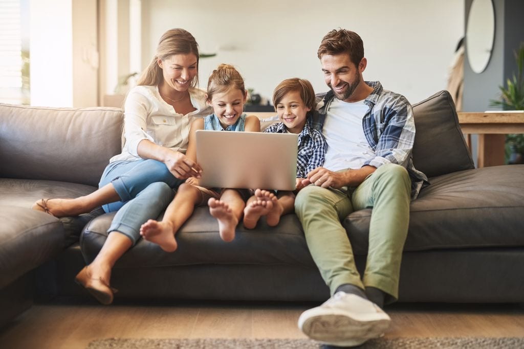 Familia, computadora portátil y niños con padres en un sofá de sala con juego educativo en línea. Mamá, papá y niños pequeños juntos con vínculos, cuidado de padres y amor en una casa viendo un video en una computadora.