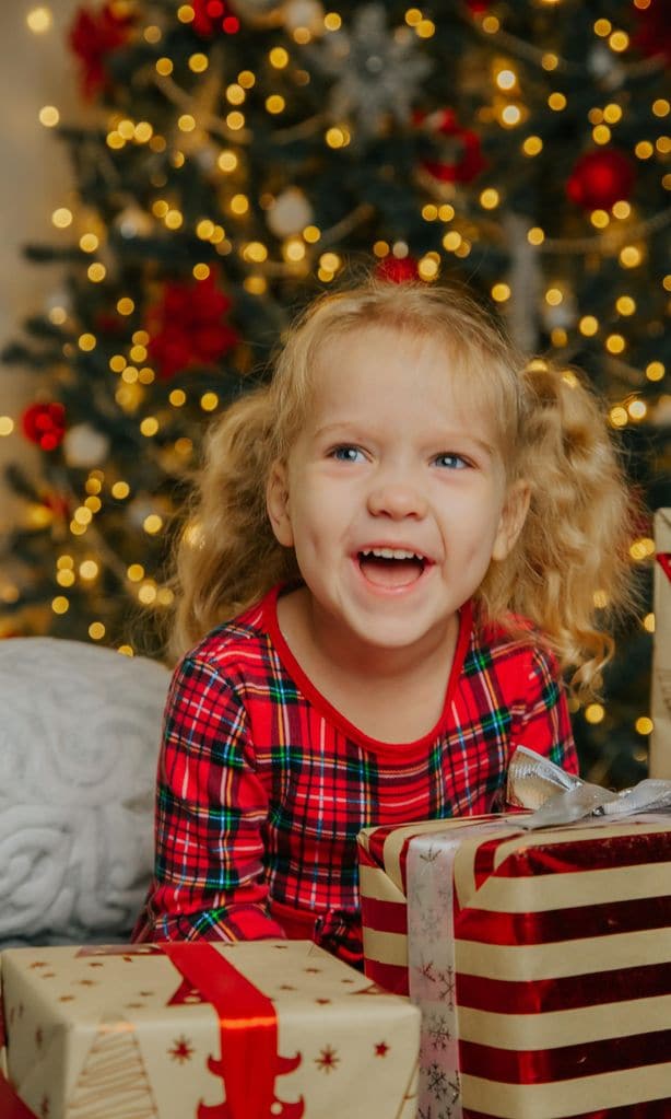 Niña ilusionada con regalos bajo el árbol de navidad