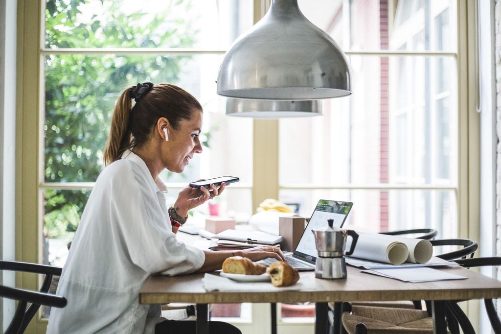 mujer desayunando mientras trabaja con su portátil y habla por teléfono