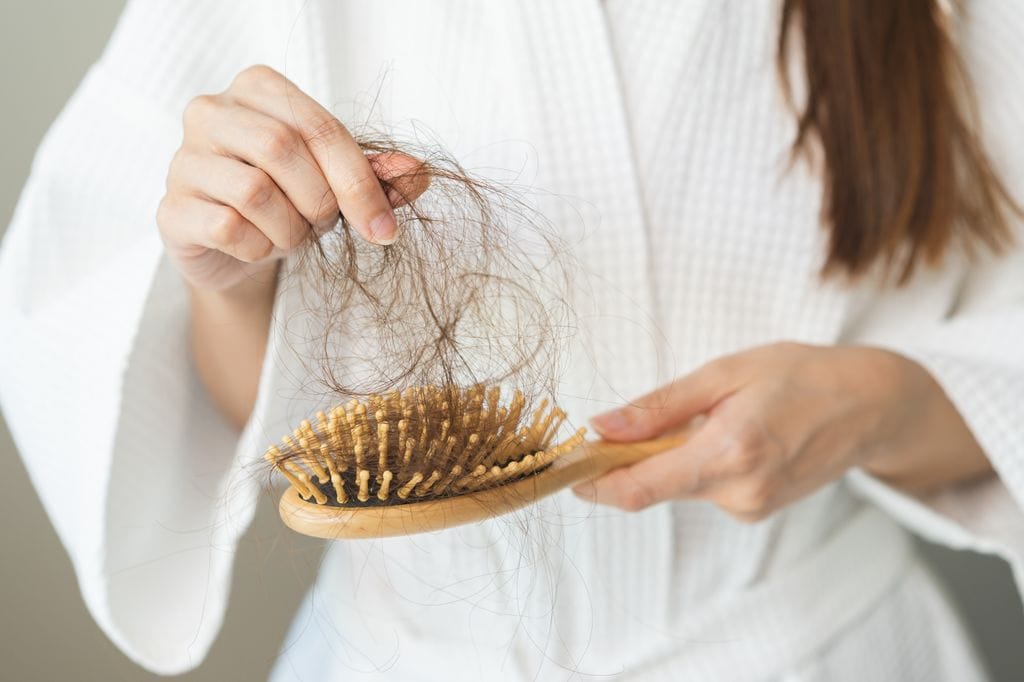 mujer recogiendo un mechón de cabello del cepillo del pelo