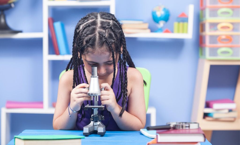 little elementary schoolgirl using microscope in classroom