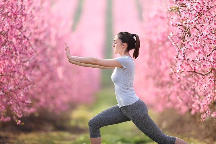 Mujer haciendo tai chi en un jardín con cerezos en flor