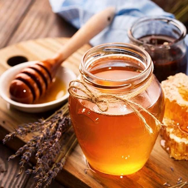 envase de vidrio con miel sobre tabla de madera