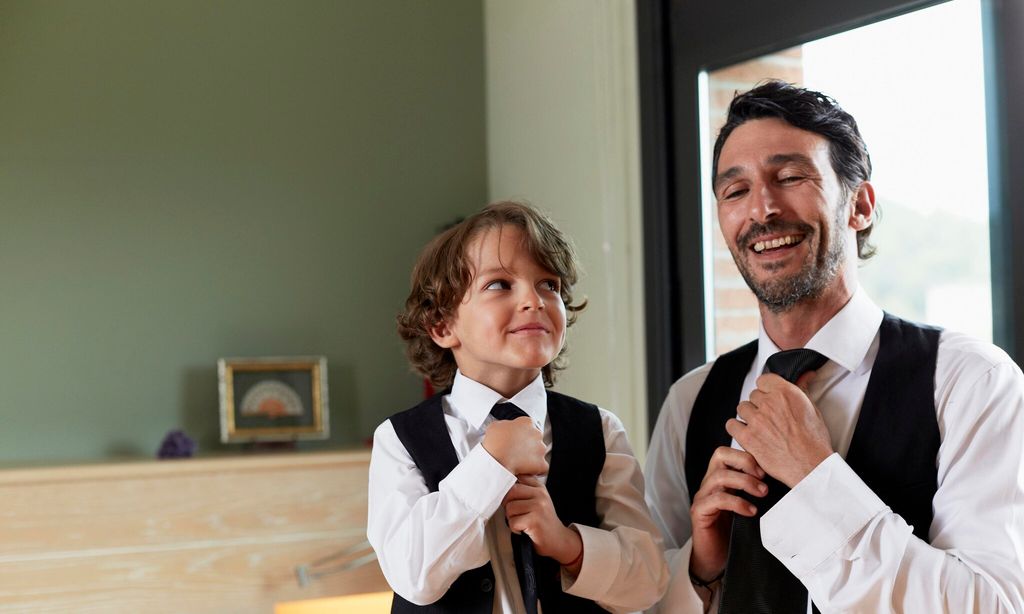 Boy adjusting tie while looking at father