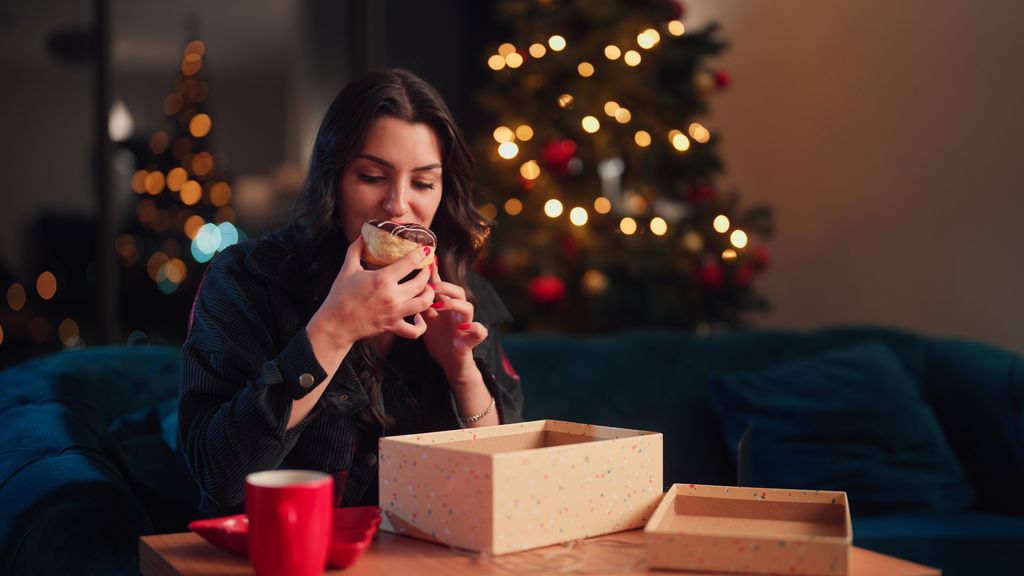 mujer en casa comiendo un dulce con el árbol de Navidad iluminado