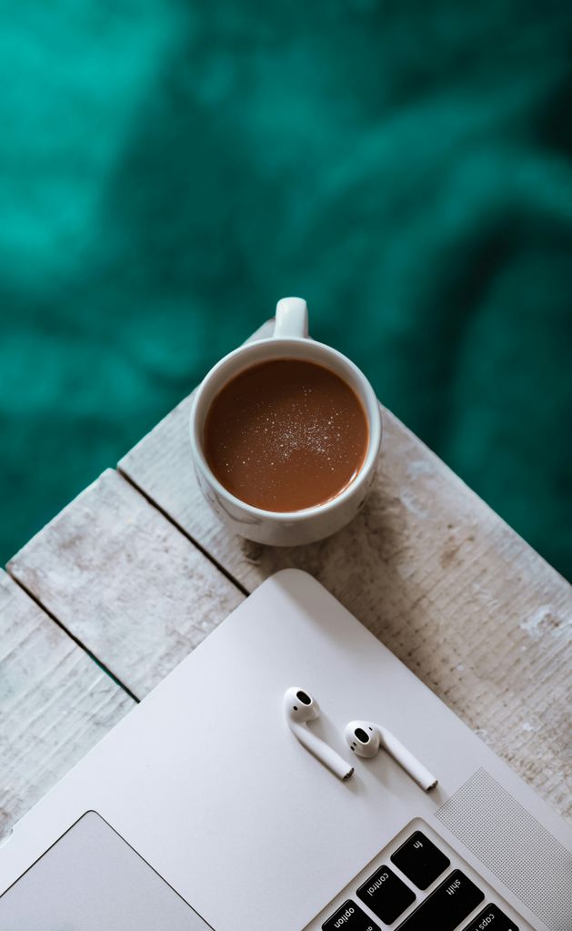 Unos AirPods en una MacBook junto a una taza de café