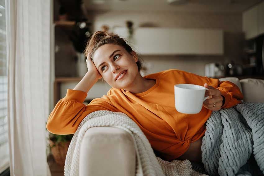 Mujer joven descansando en el sofá con una taza de té.