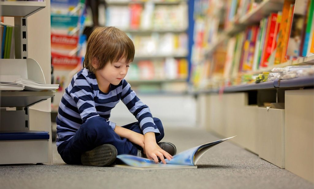 adorable little child boy sitting in a book store reading books