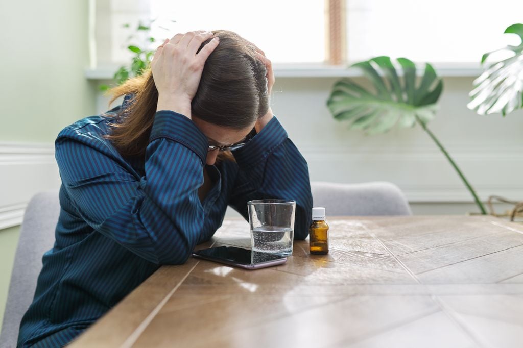 mujer deprimida con unas pastillas y un vaso de agua sobre la mesa