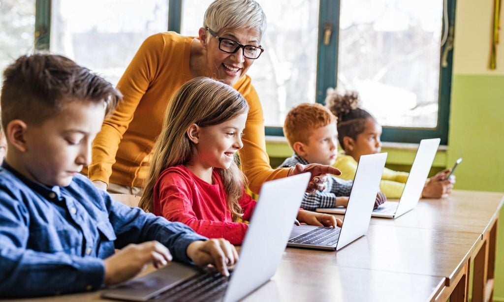 happy mature teacher assisting her students on computer class at school 