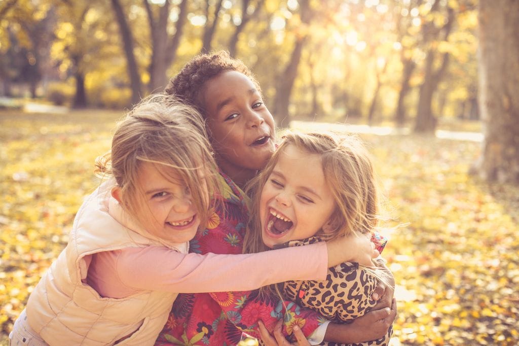 Tres niños abrazándose al aire libre, en el contexto de frases de paz para niños