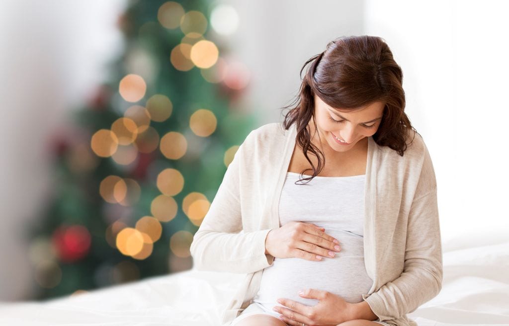 Embarazada tocándose la tripa con árbol de Navidad al fondo