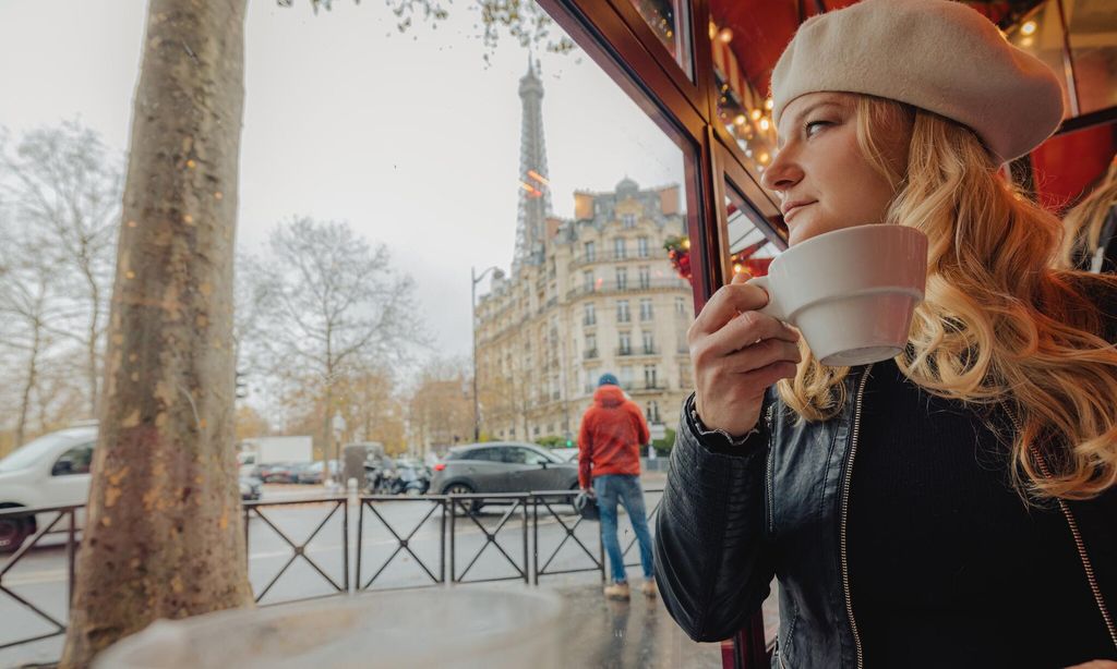 Woman sitting in a French cafe in Paris, looking outside the window while holding a cup of Coffee