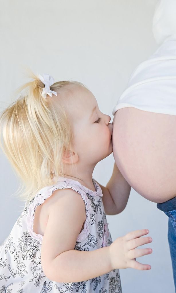 Niña dando un beso a una barriga de embarazada