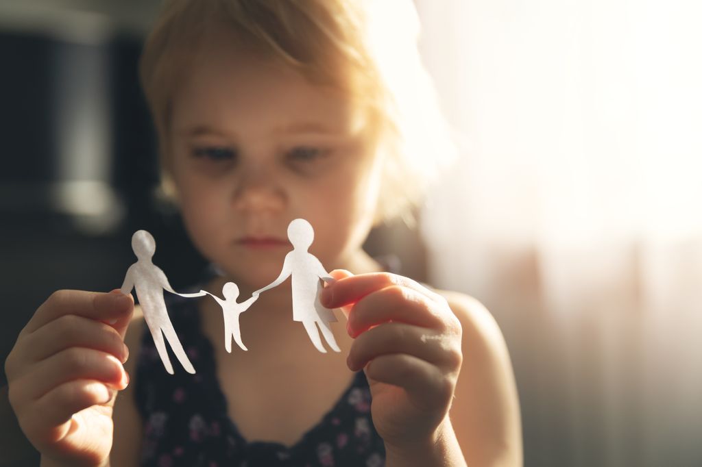 Niña con un recortable de papel de familia con actitud triste en contexto de custodia compartida