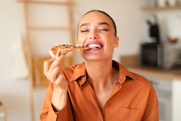 mujer comiendo una porción de pizza