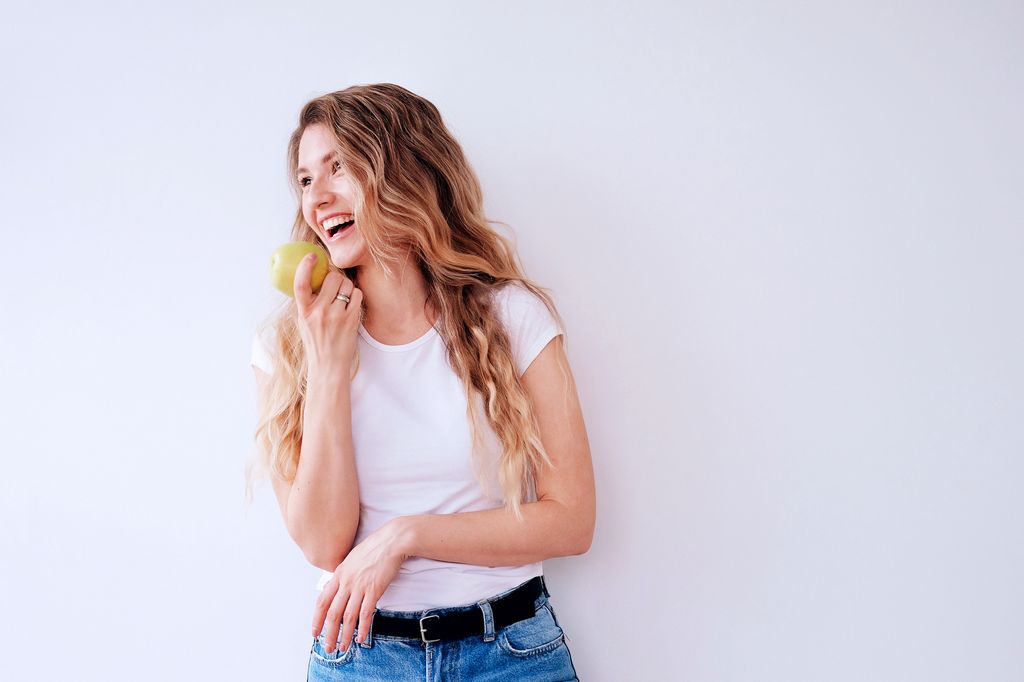 mujer sonriente con el pelo largo comiéndose una manzana