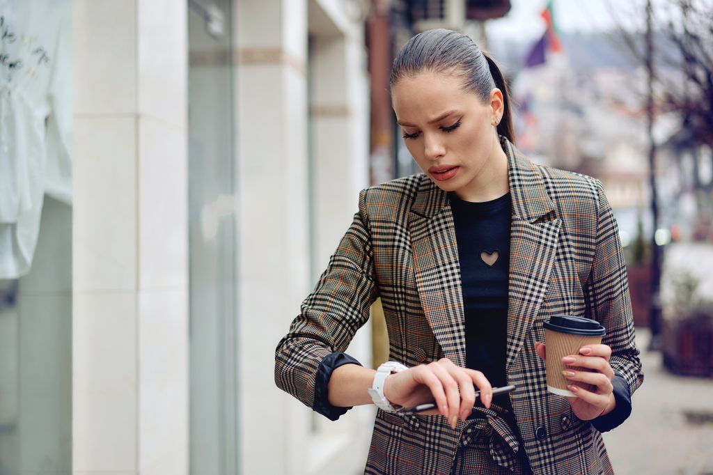 mujer joven por la calle mirando su reloj con cara de preocupación