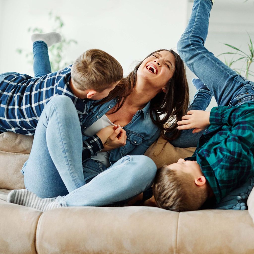 Madre riendo con sus hijos en el sofá de casa.