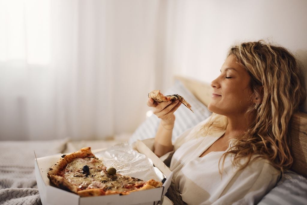 mujer comiendo pizza en la cama