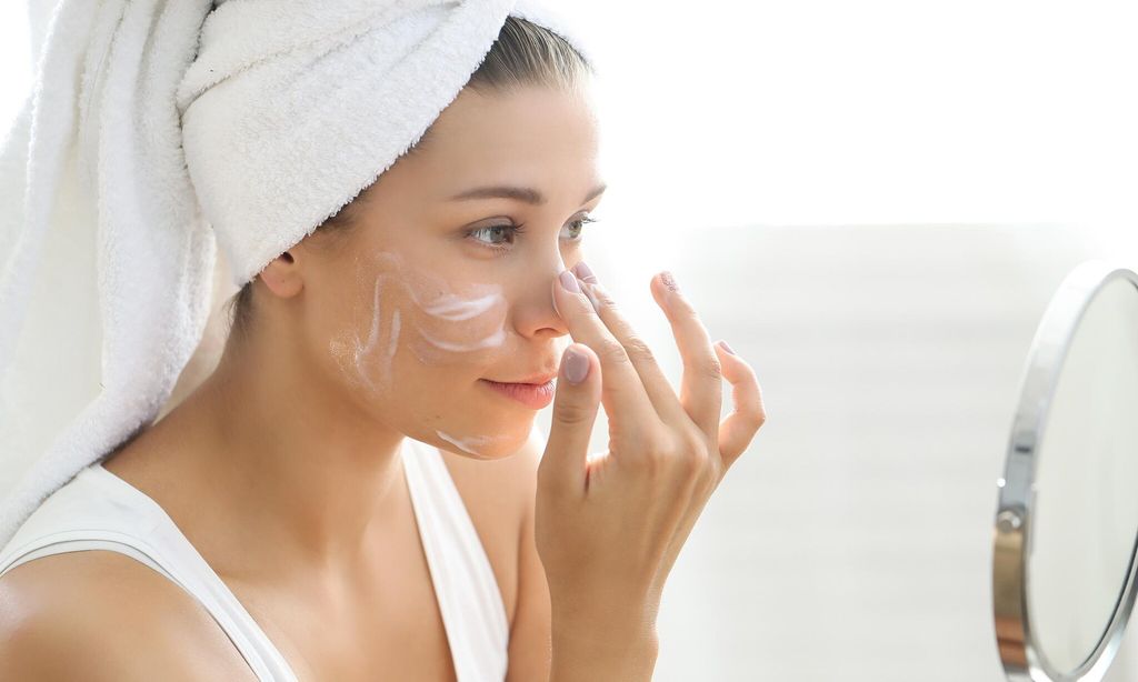 mujer colocando crema en su rostro frente a un espejo