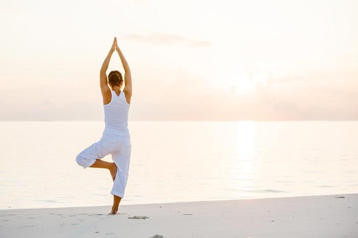 mujer haciendo yoga en la playa