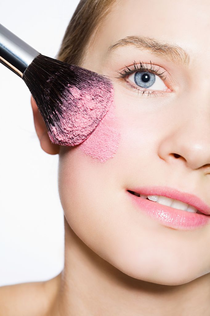 Foto cortada de rostro de mujer aplicando colorete rosa con una brocha gruesa