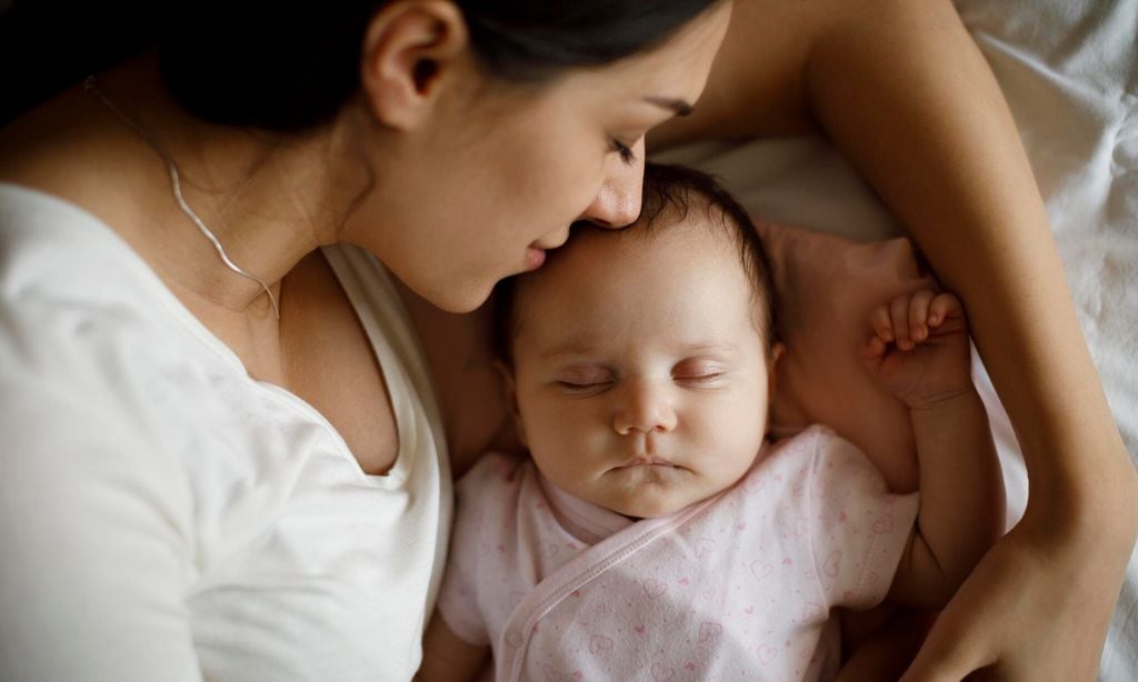 Beautiful young mother and her cute little baby sleeping in bed at home