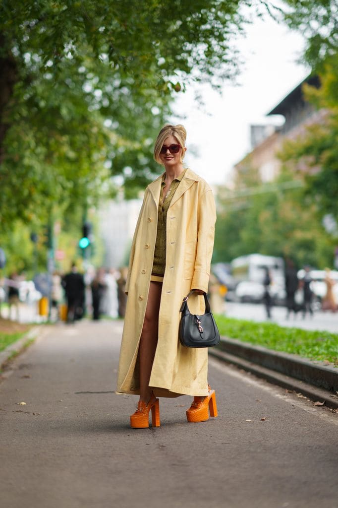 Xenia Adonts con una gabardina beige sobre un vestido de punto verde abotonado, zapatos de plataforma naranja, gafas de sol rojas, un bolso negro es vista fuera de Gucci durante la Semana de la Moda de Milán Menswear Primavera/Verano 2025 el 20 de septiembre de 2024 en Milán, Italia. 